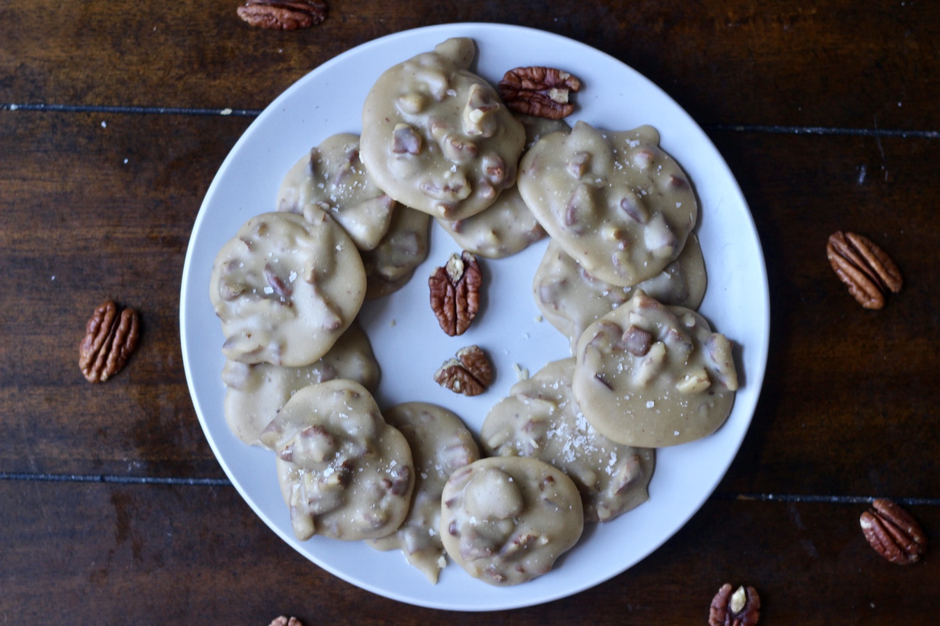 Circle of pralines on a white plate with extra pecans sprinkled around.