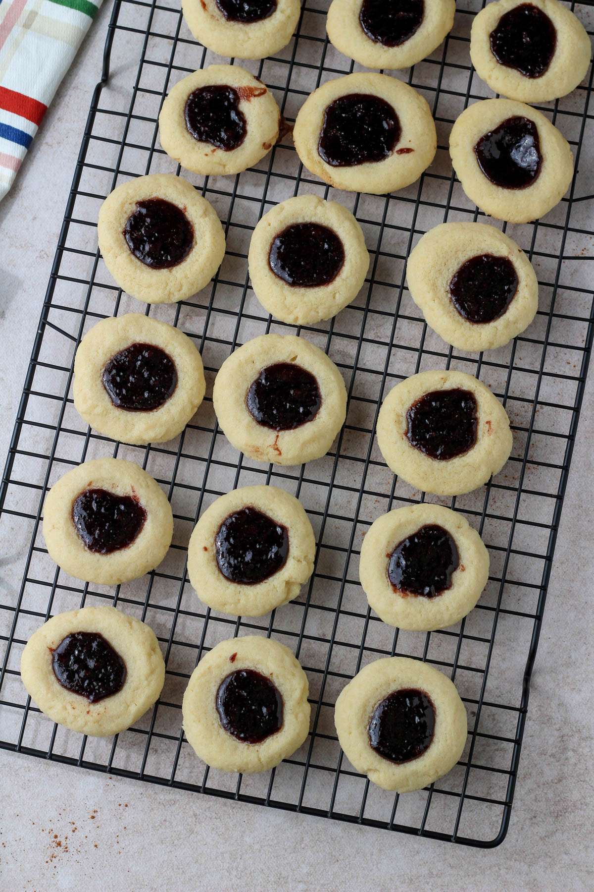A black cooling rack with spiced blackberry thumbprint cookies.