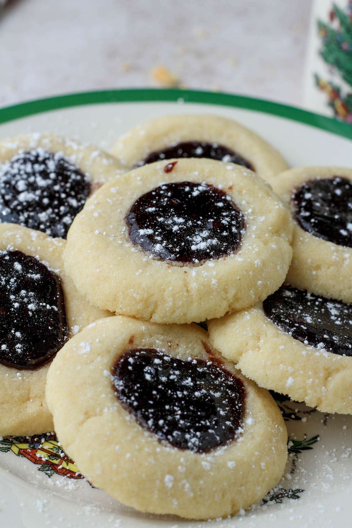 A close up of a white plate with a green rim topped with powdered sugar dusted thumbprint cookies.