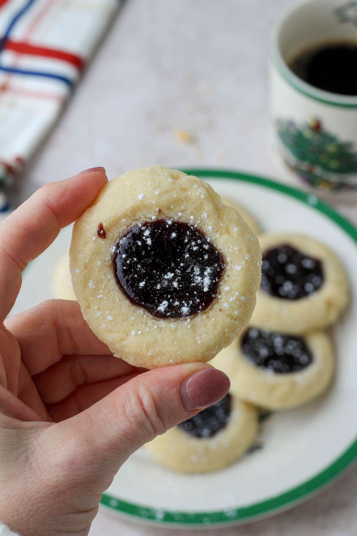 A hand holding a dairy-free spiced thumbprint cookie over a white and green plate topped with thumbprint cookies.