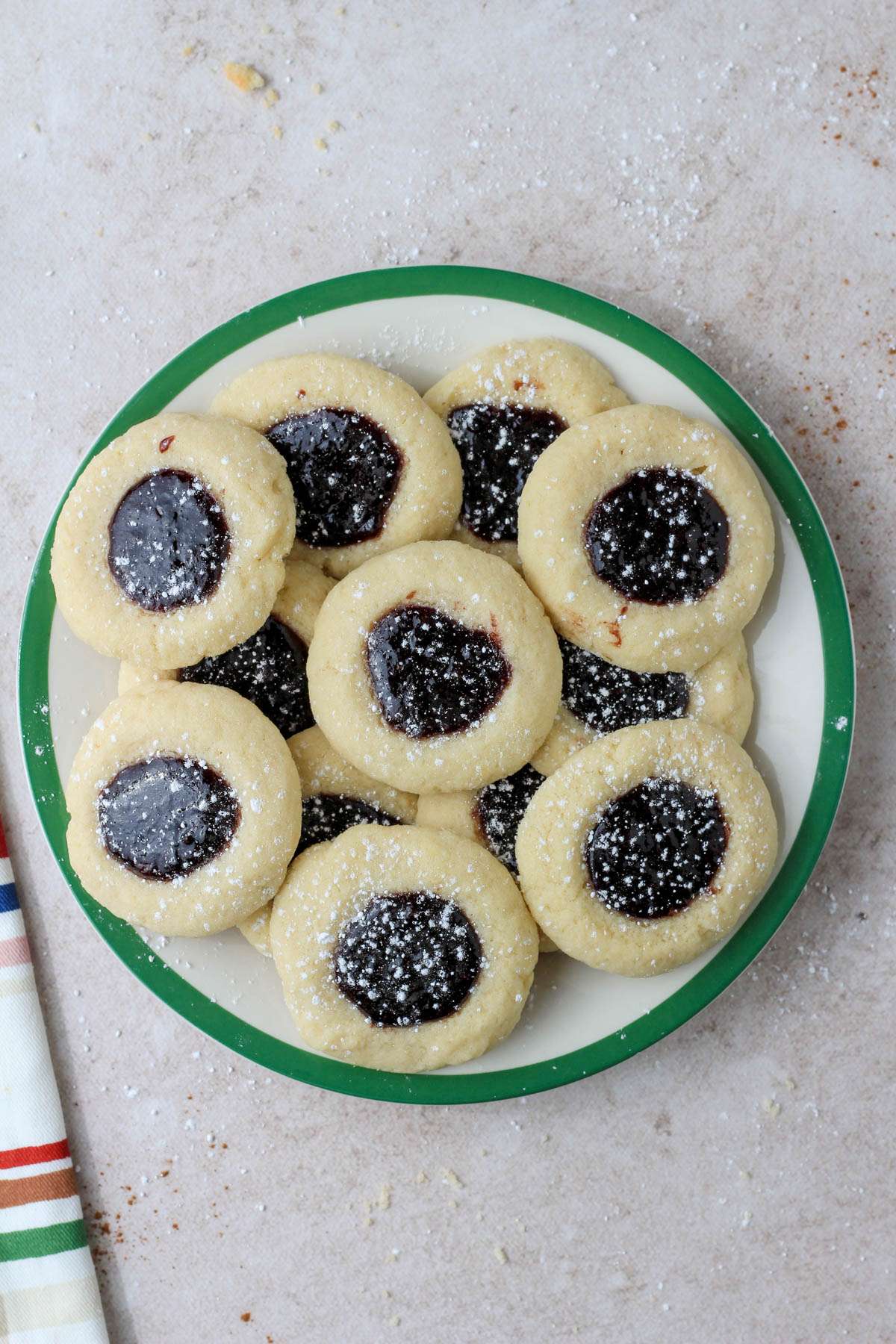 A green rimmed plate with a pile of spiced blackberry thumbprint cookies dusted with powdered sugar.