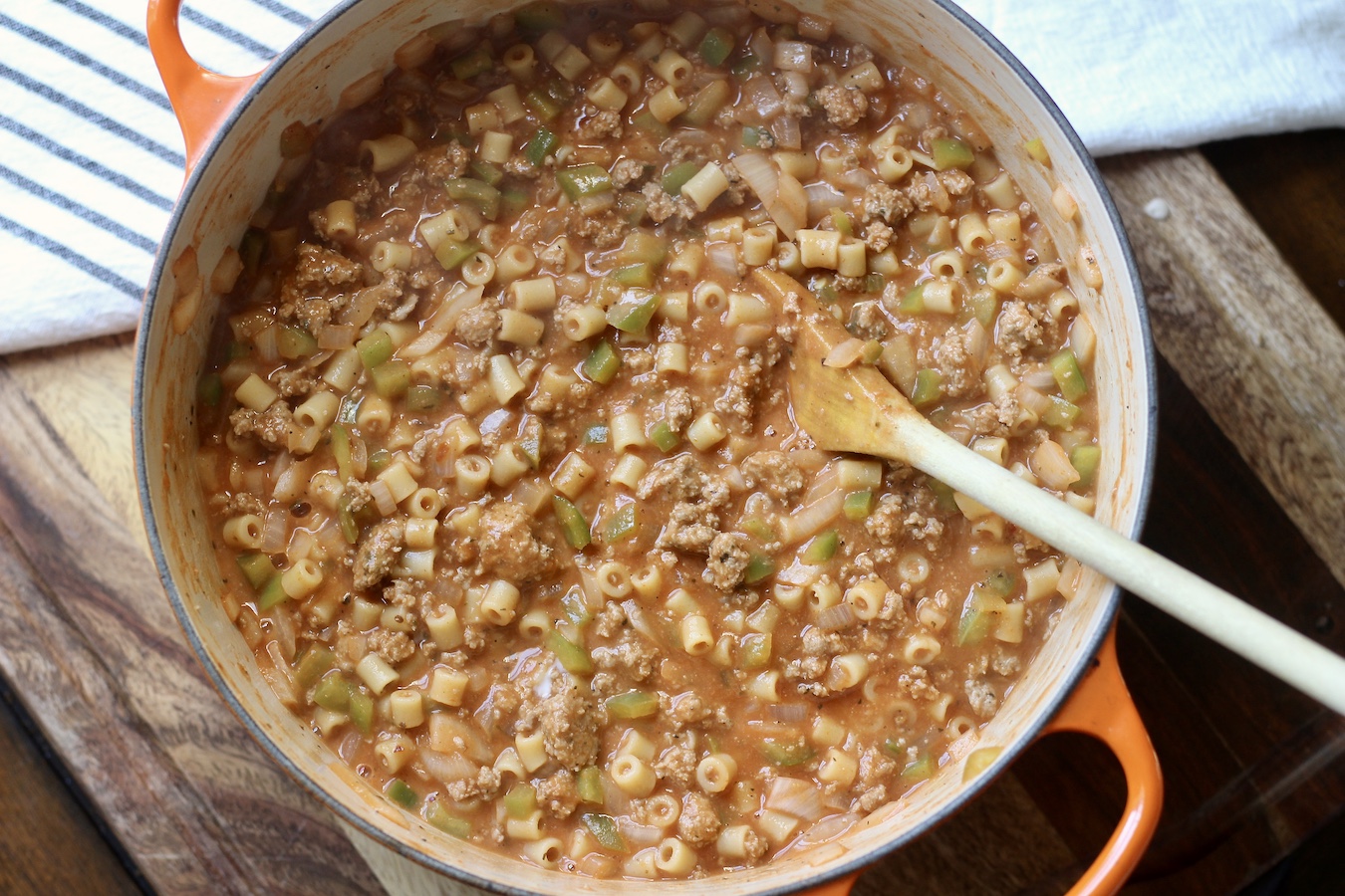 An orange pot of Turkey Mac with a wooden spoon on a wooden counter.