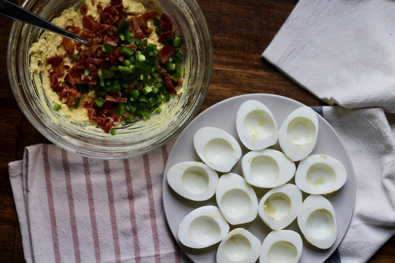 A glass bowl with deviled egg filling and a white plate with hard boiled egg halves on a white and pink striped dish towel.