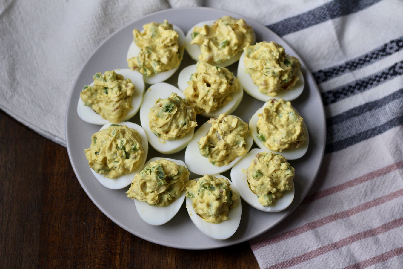 A white plate with Bacon Jalapeno Deviled Eggs on a blue, pink, and white striped dish towel.