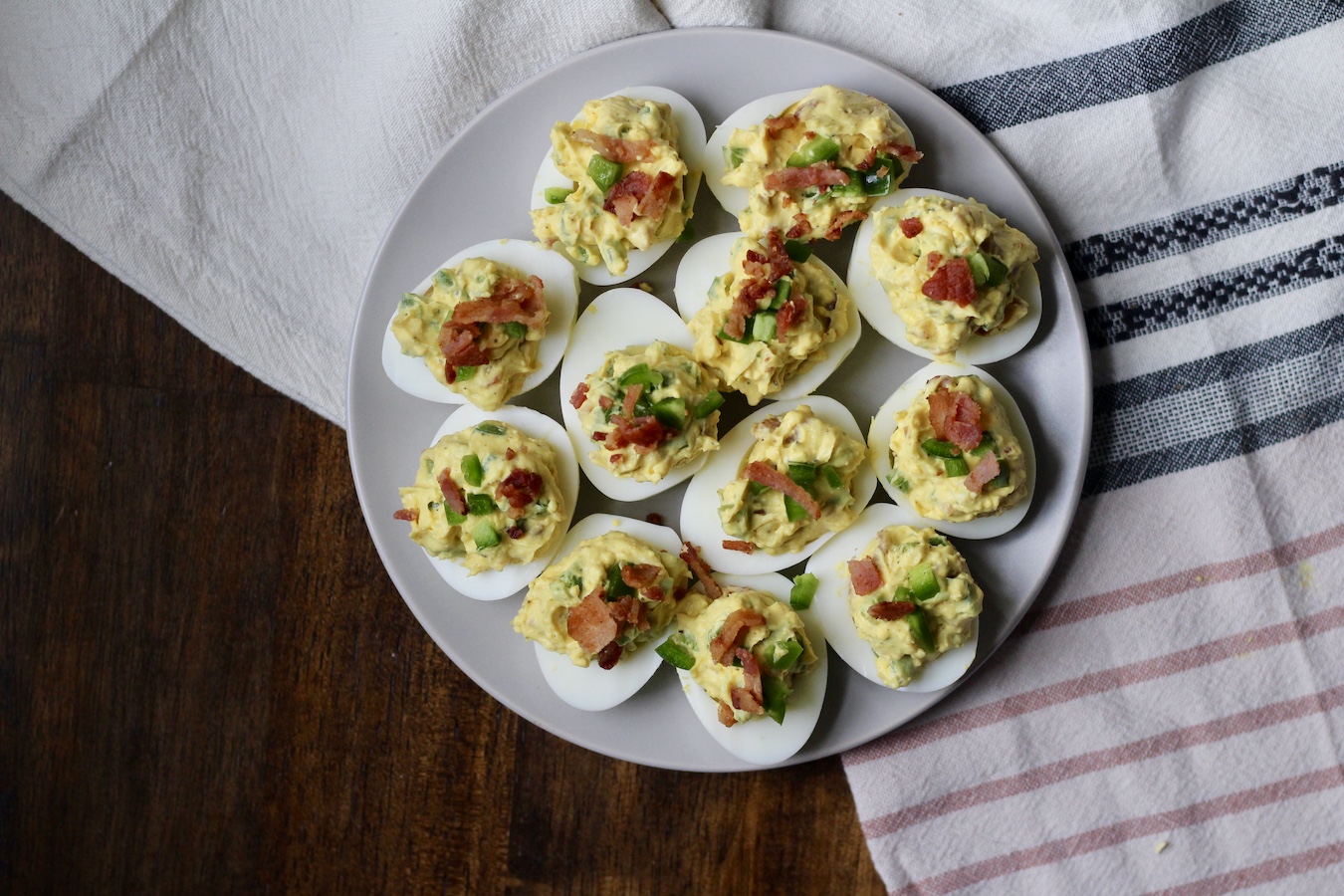A white plate with Bacon Jalapeno Deviled Eggs on a blue, pink, and white striped dish towel.