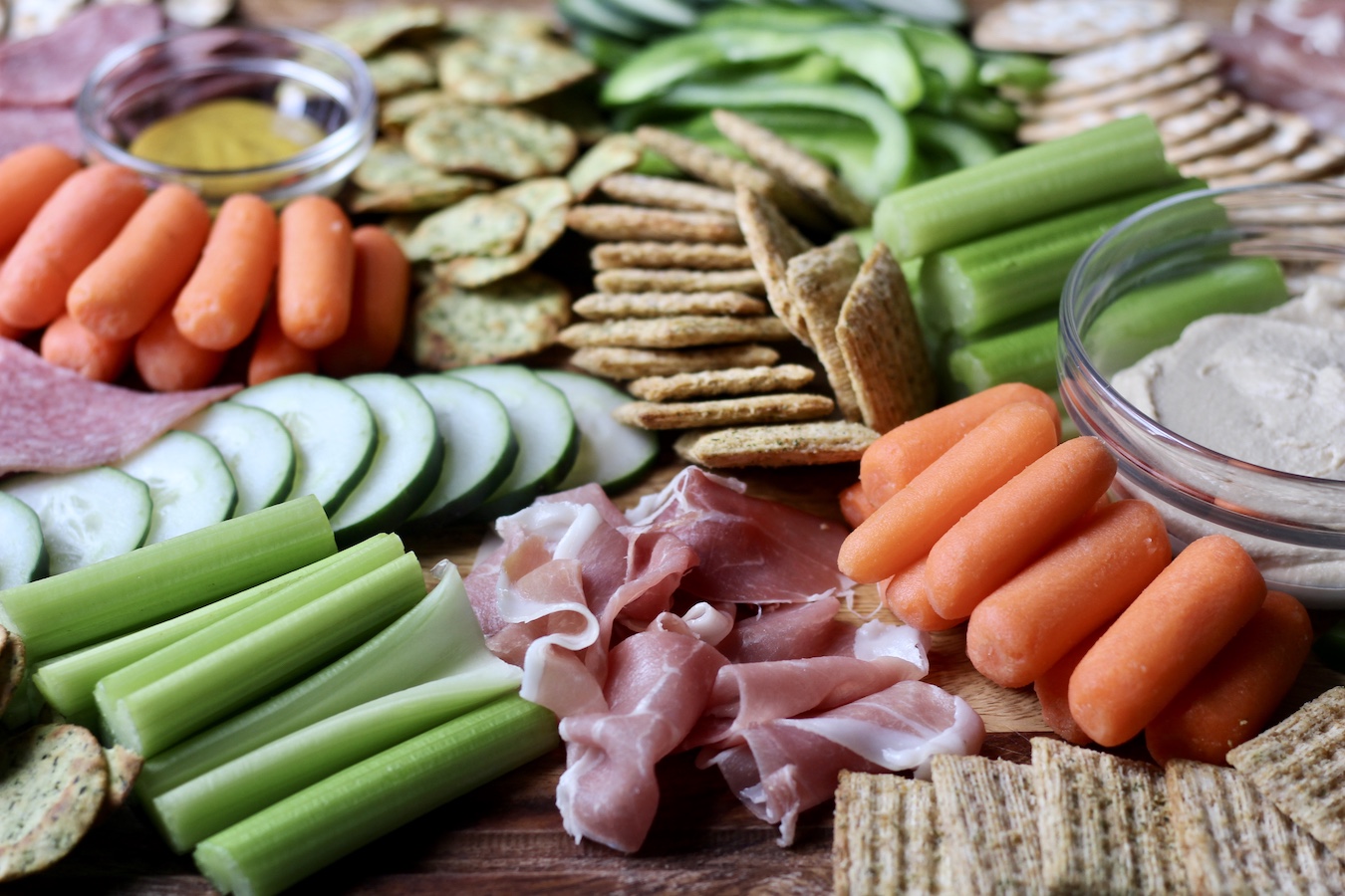Image of Charcuterie Board with meat in the front, vegetables and crackers around it. 