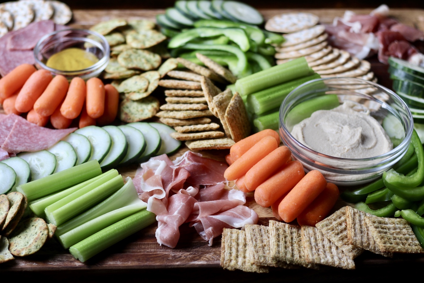 Charcuterie Board with hummus, crackers, vegetables, meats, and honey mustard. 