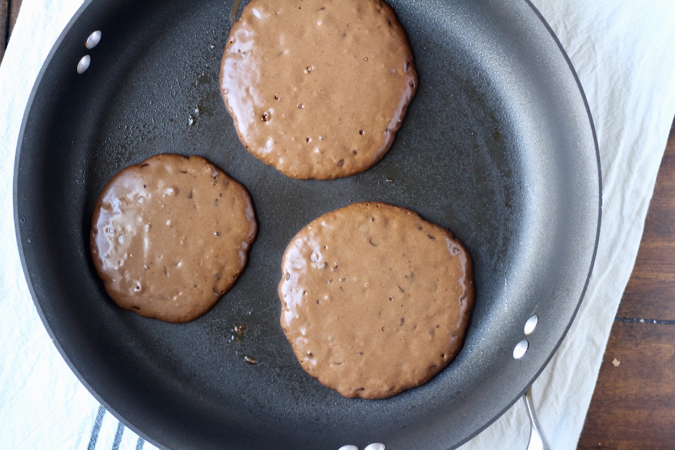 Three double chocolate chip pancakes cooking in a non-stick skillet.