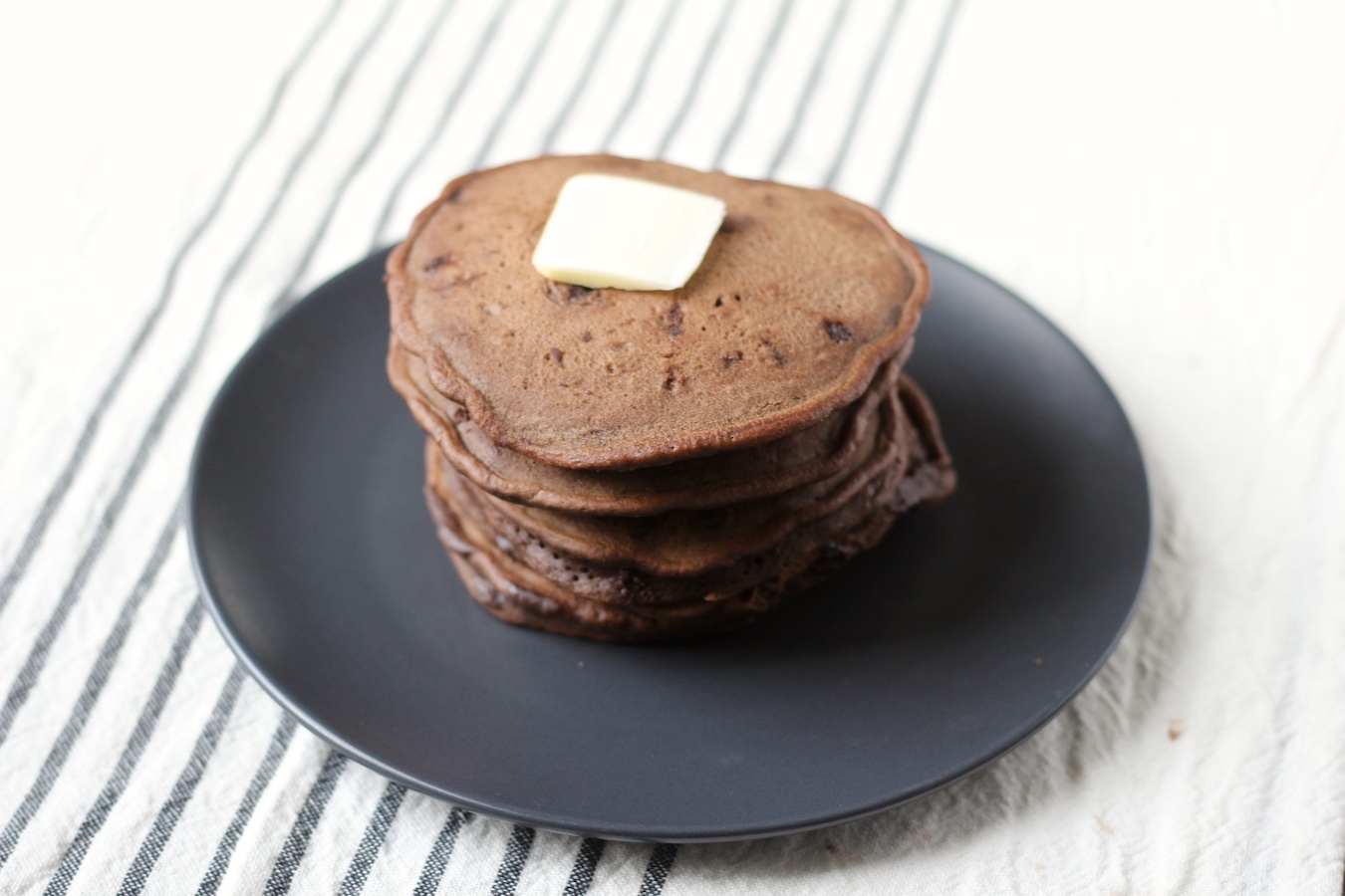 A stack of 5 pancakes on a blue plate on a white and blue striped dish towel.