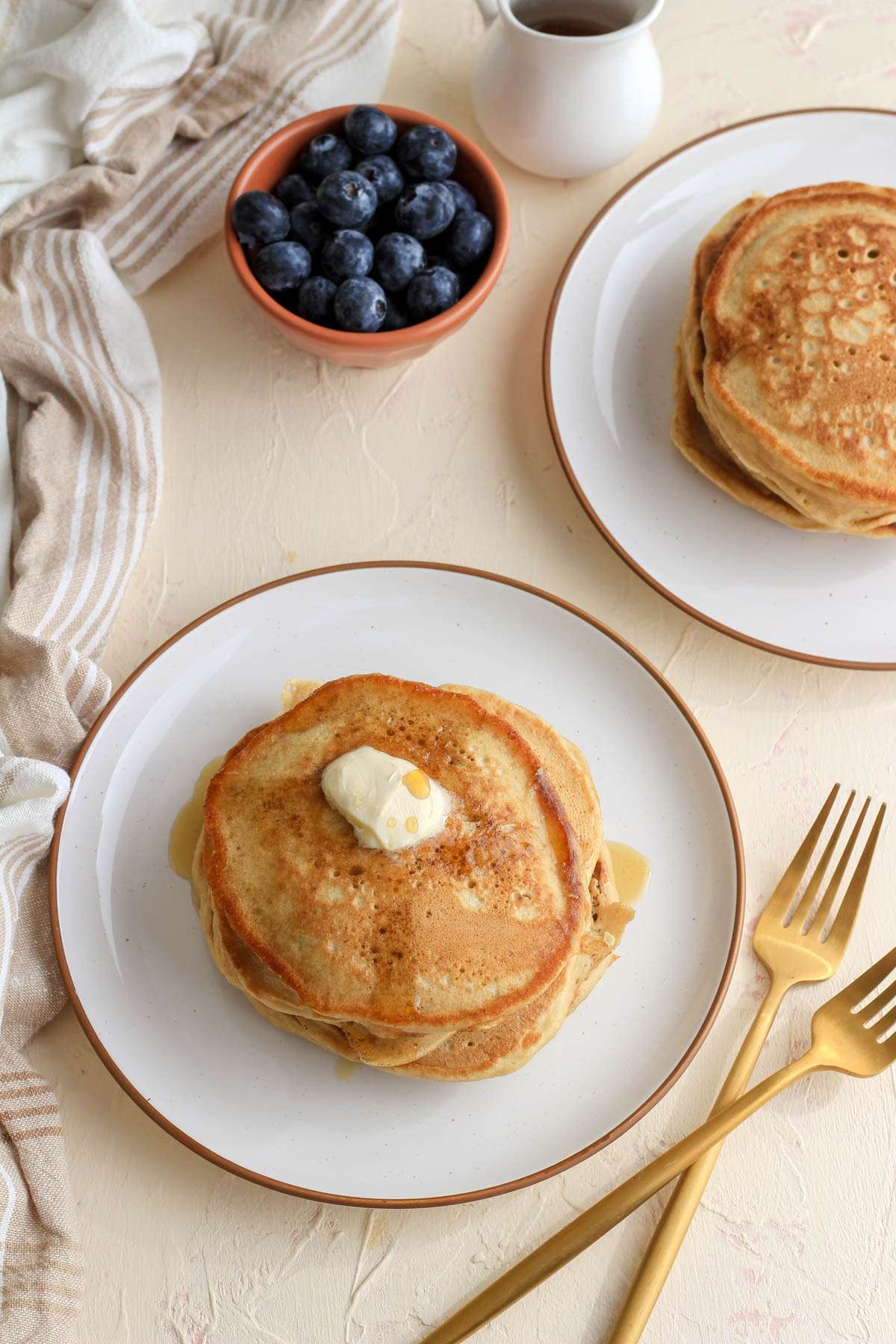 A top down image of a stack of buttermilk pancakes with a pad of vegan butter and a drizzle of maple syrup.