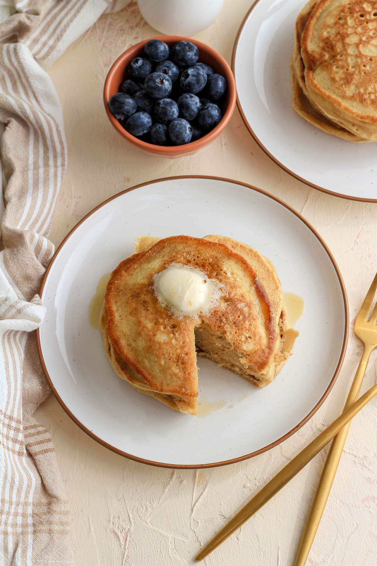 A top down image of a stack of buttermilk pancakes on a white plate with a wedge taken out of the stack.