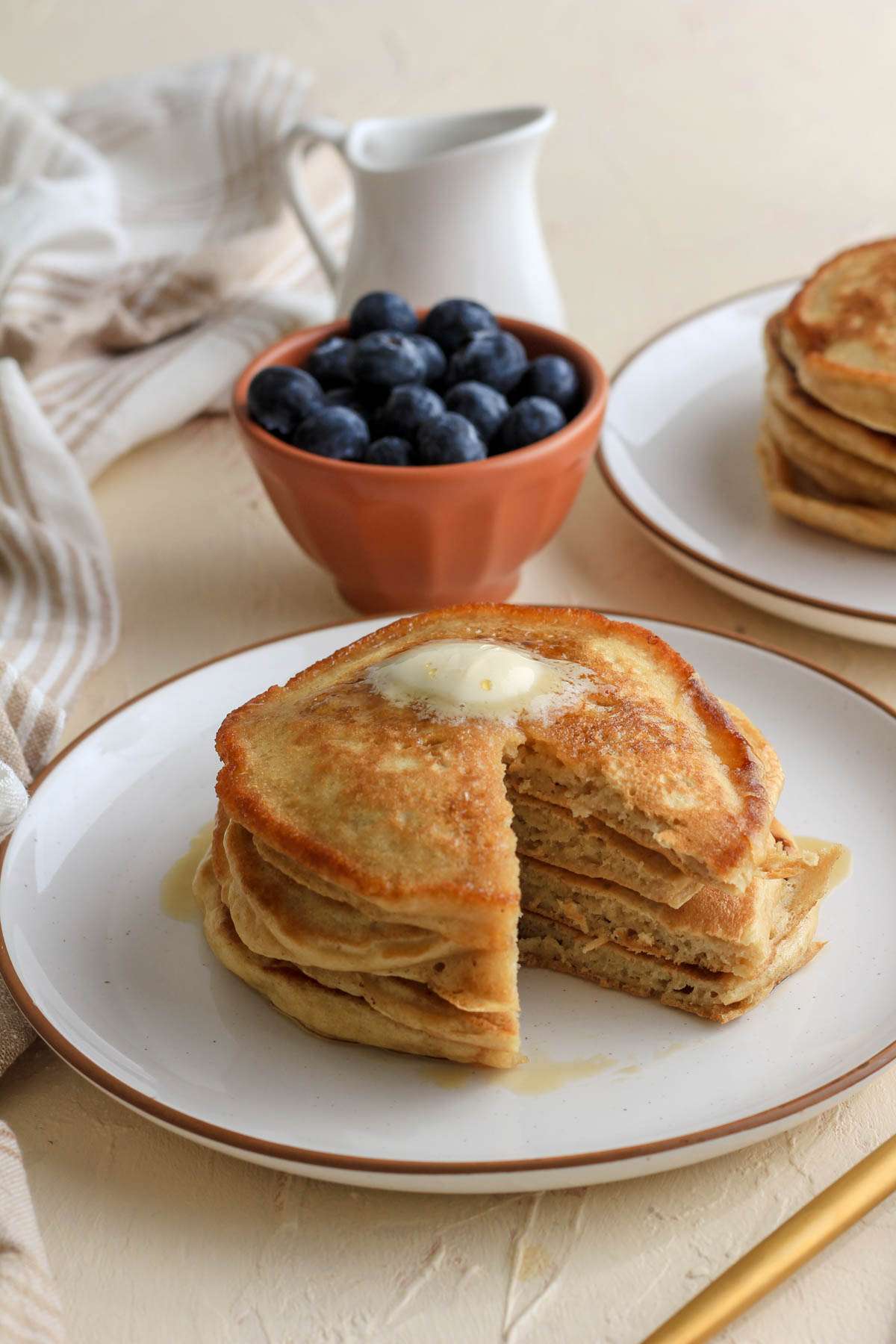 From the side image of dairy free buttermilk pancakes on a white plate with a brown rim with a wedge missing and a pat of vegan butter on top.