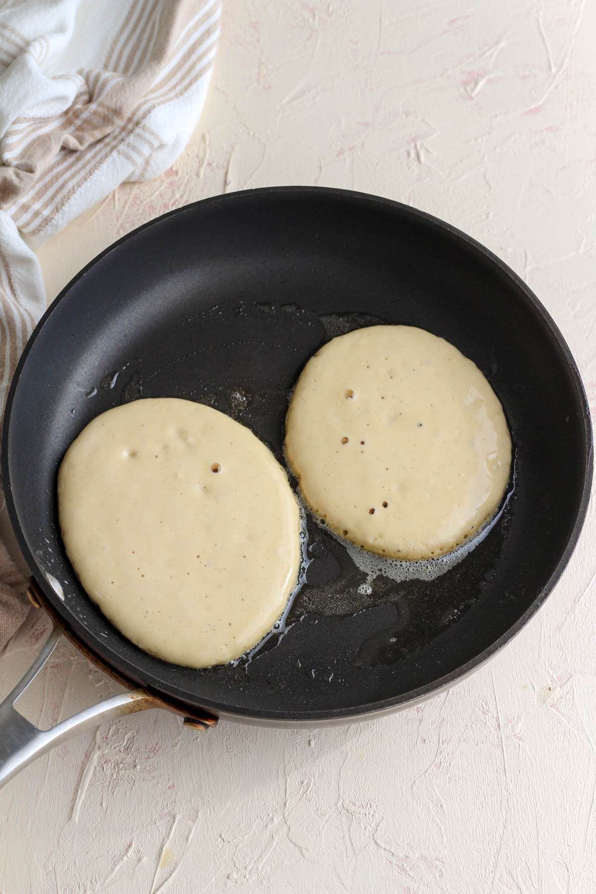 A non-stick skillet with two dairy free buttermilk pancakes cooking.