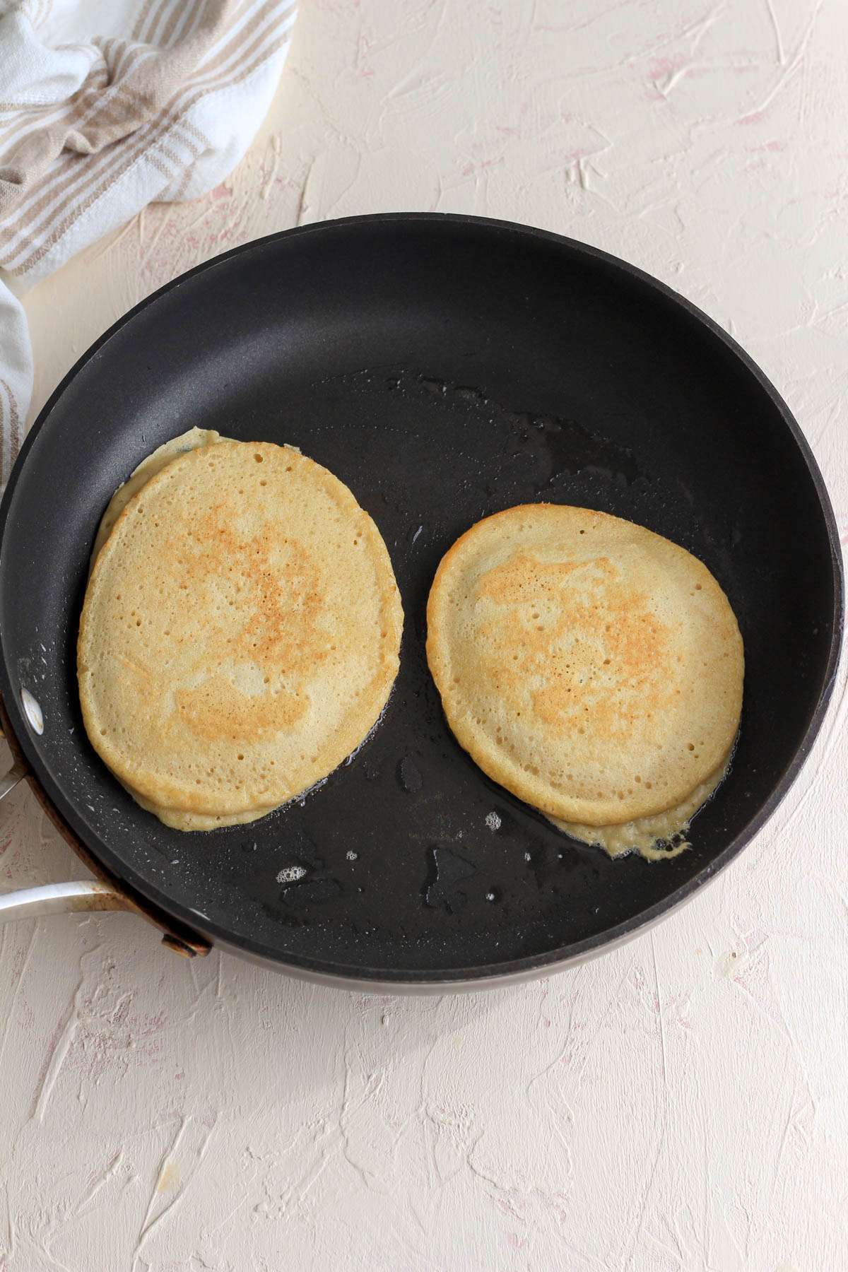 A non-stick skillet with two dairy free buttermilk pancakes cooking on the other side.