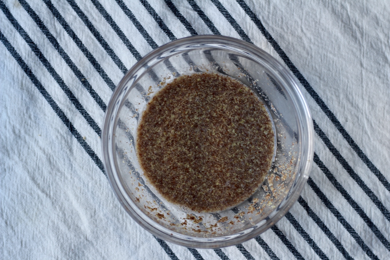Flax meal soaking in a bowl of water on a blue and white dish cloth.