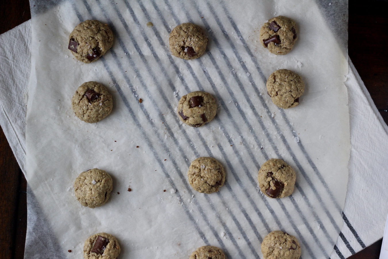 Baked lactation cookies on a parchment paper on a white and blue striped dish towel.