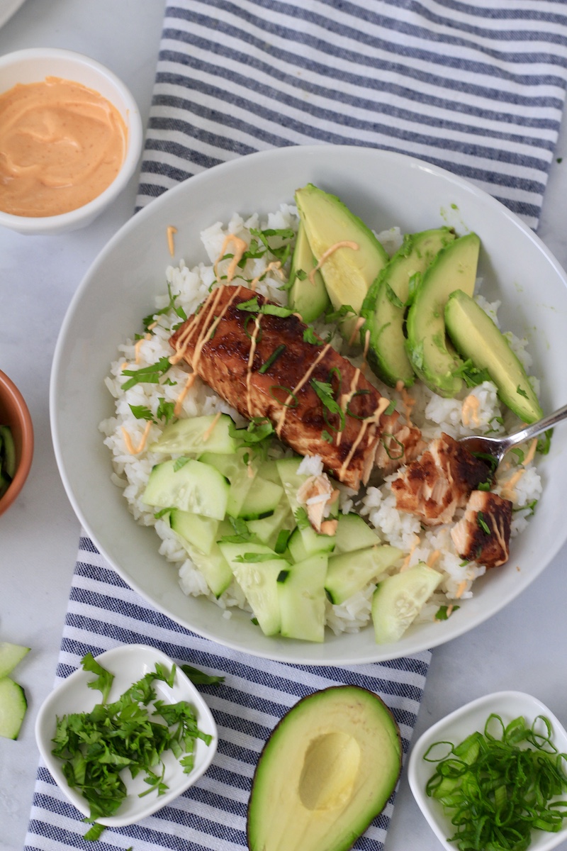 A salmon avocado bowl topped with the sauce on a white and blue striped towel.