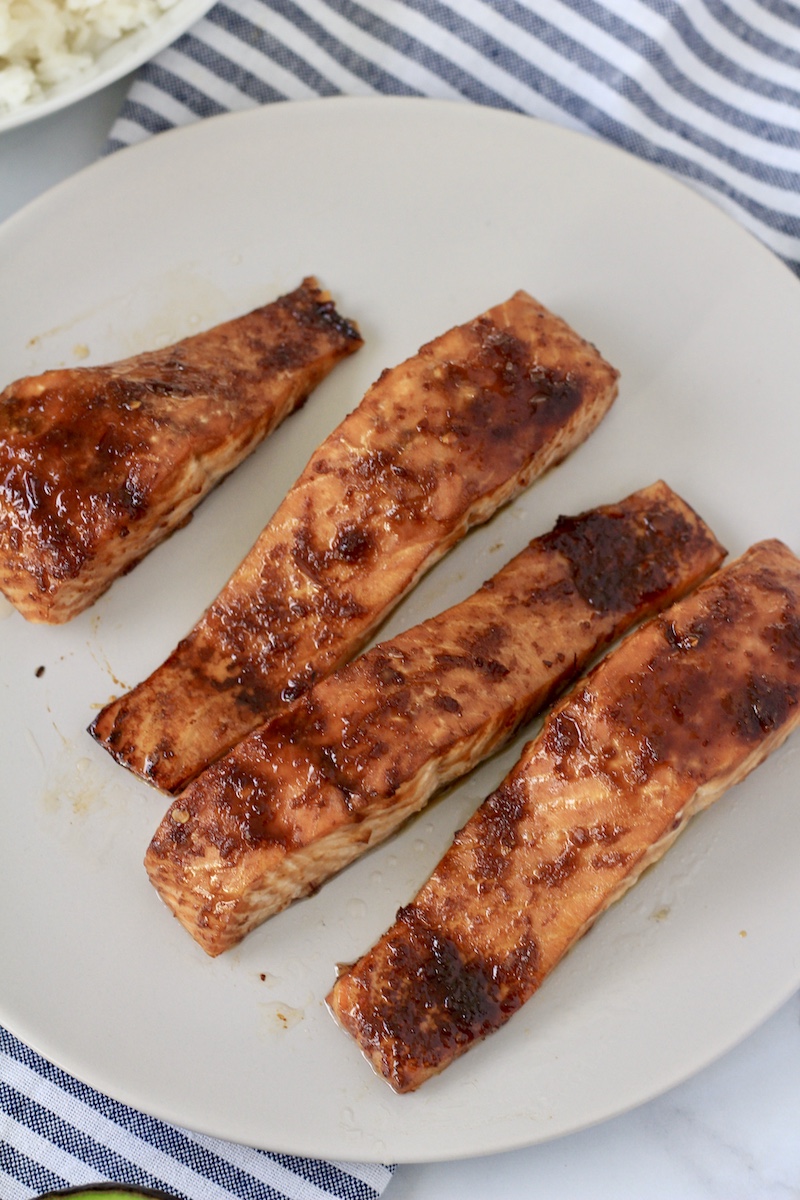 Oven baked salmon fillets on a white plate on a counter with a blue and white striped dish towel.