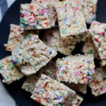 Cut funfetti rice crispy treats on a blue plate on a white and blue dish towel.