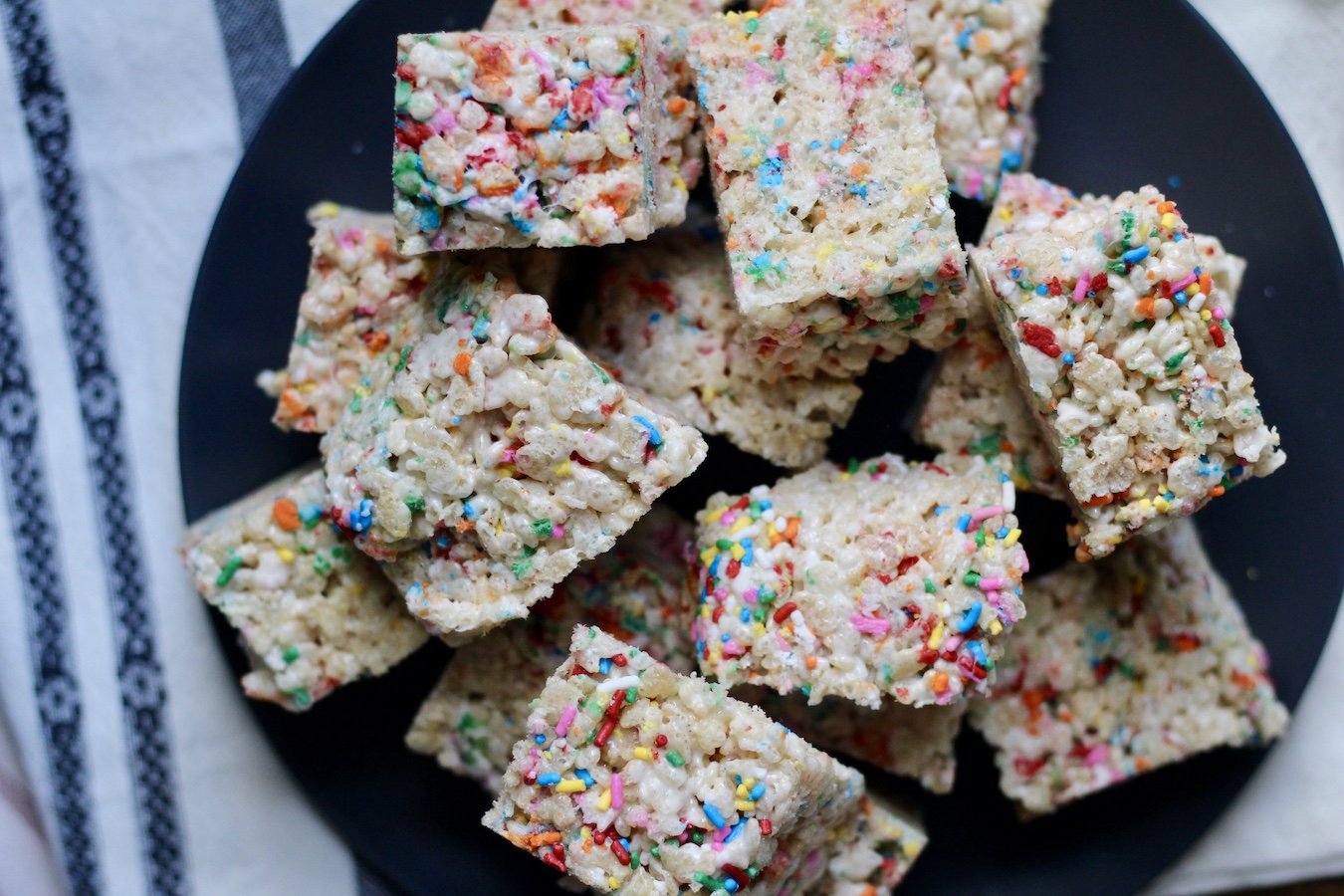 Cut funfetti rice crispy treats on a blue plate on a white and blue dish towel.
