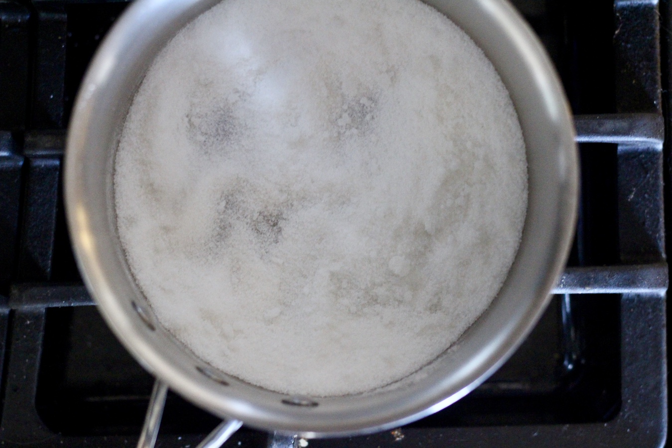 Silver pot with sugar cooking over medium low heat on a stove.