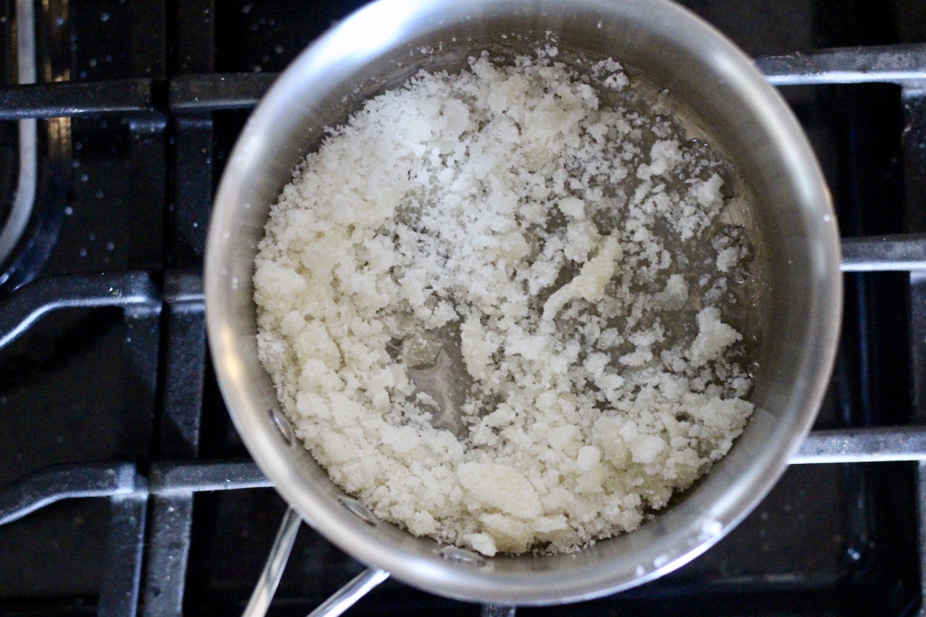 Silver pot with sugar cooking over medium low heat on a stove.