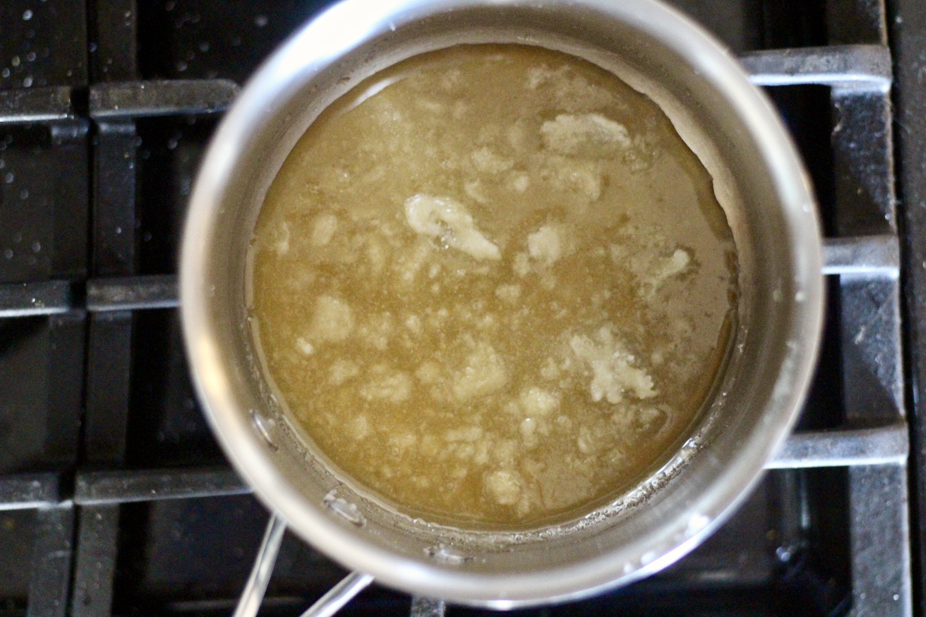 Silver pot with melted sugar cooking over medium low heat on a stove.