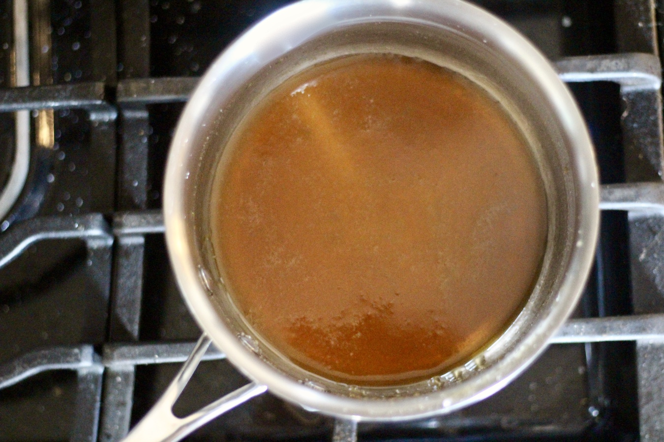 Silver pot with dark caramel colored melted sugar cooking over medium low heat on a stove.