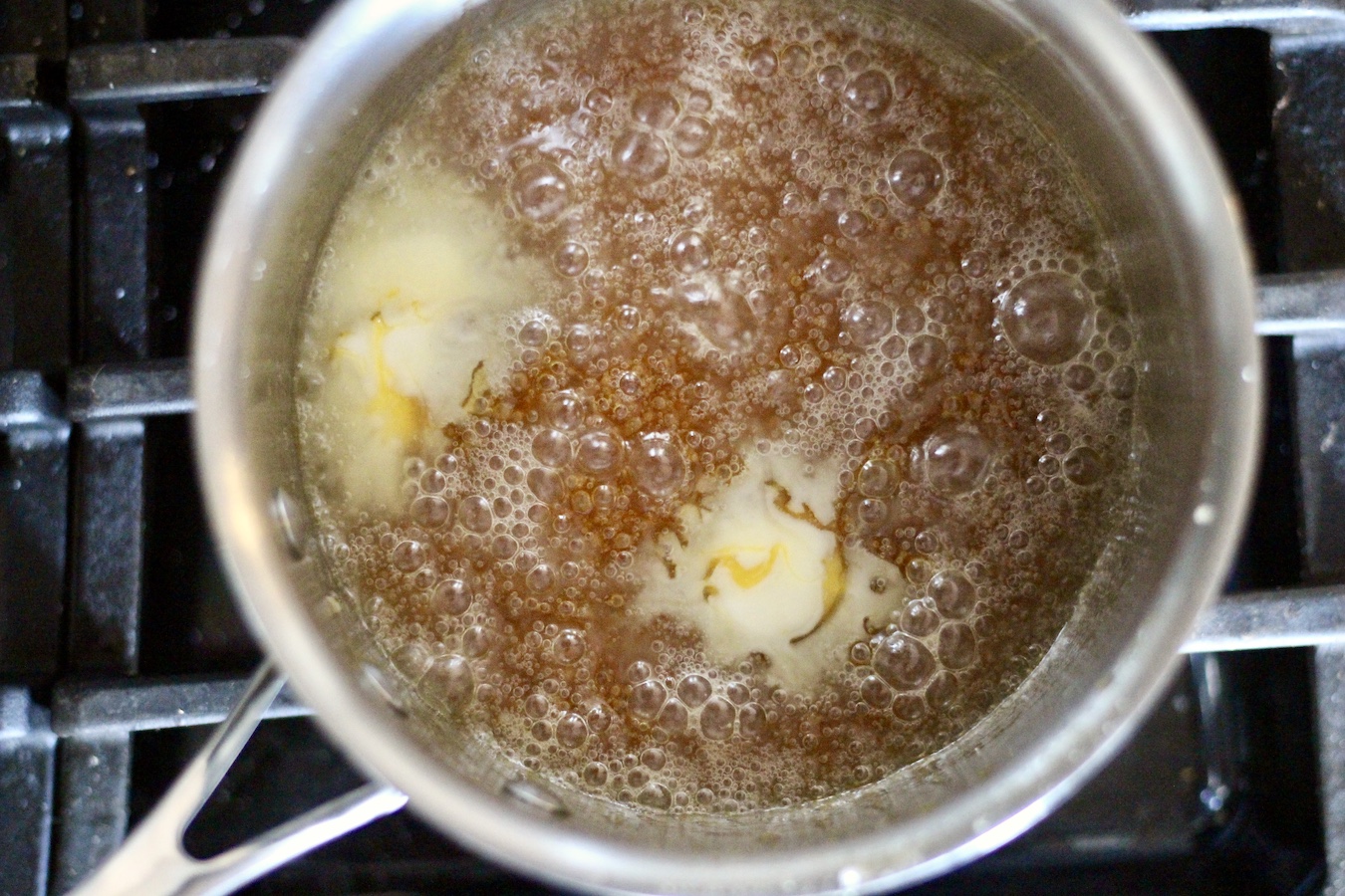 Silver pot with melted sugar and butter boiling over medium low heat on a stove.