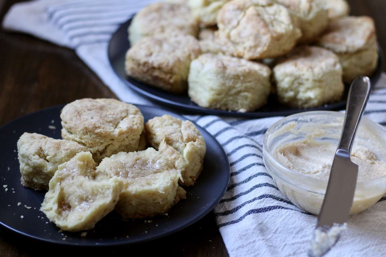 Biscuits on a small and large blue plate with honey butter to the right on a white and blue dish towel.