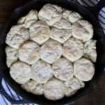 Baked skillet biscuits in a cast iron skillet on a white and blue dish towel on a wooden table.