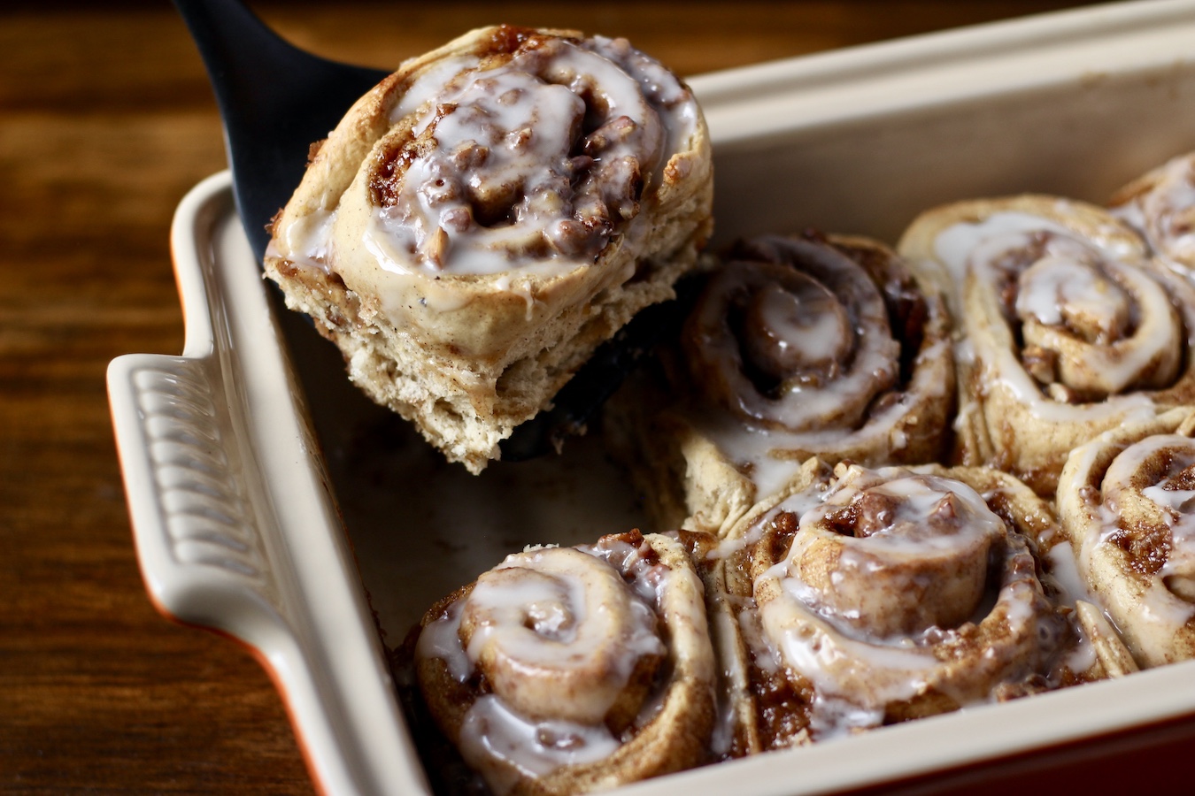A banana bread cinnamon roll on a spatula coming out of the baking dish.