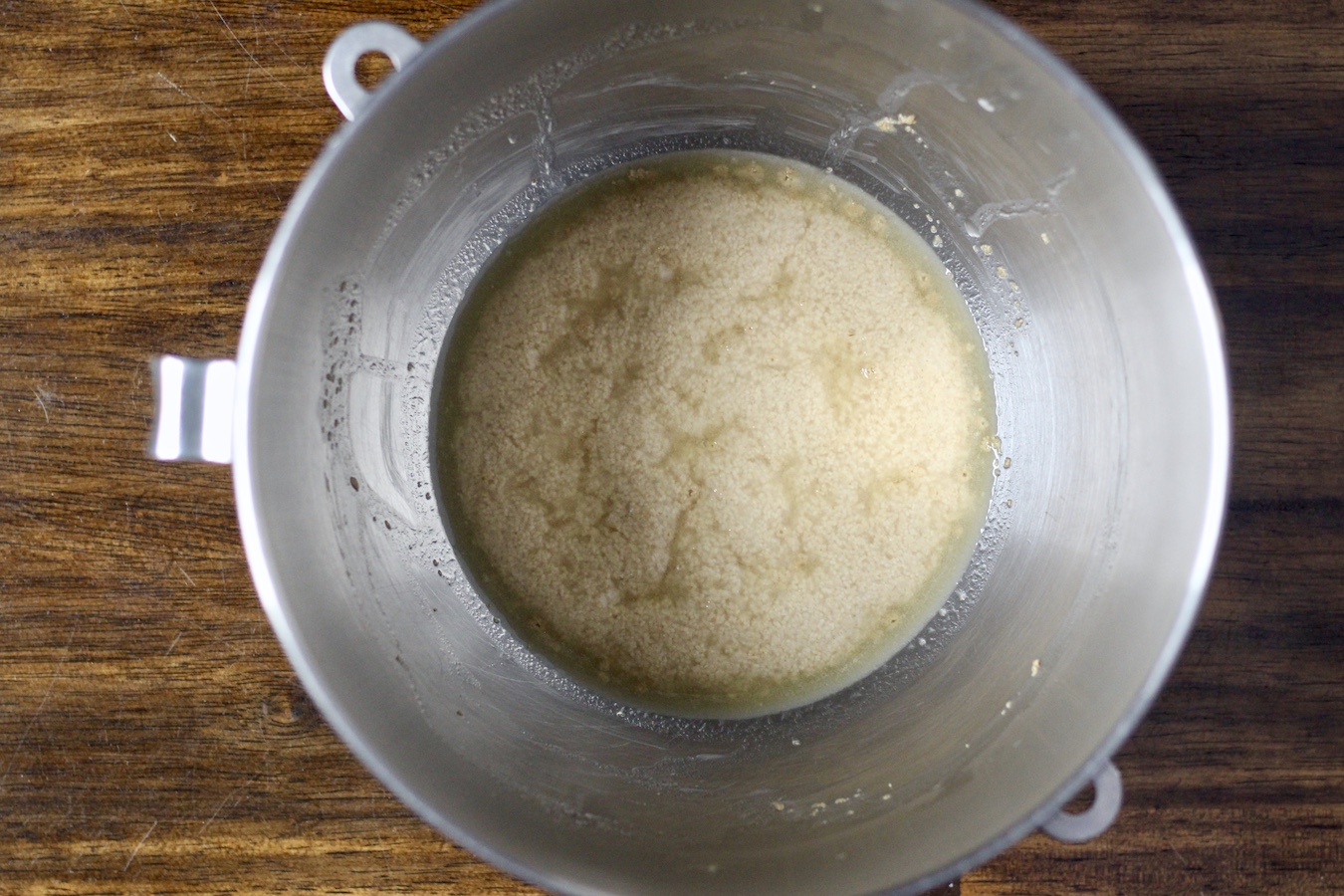 Activating the yeast in the bottom of a mixing bowl on a wooden table.
