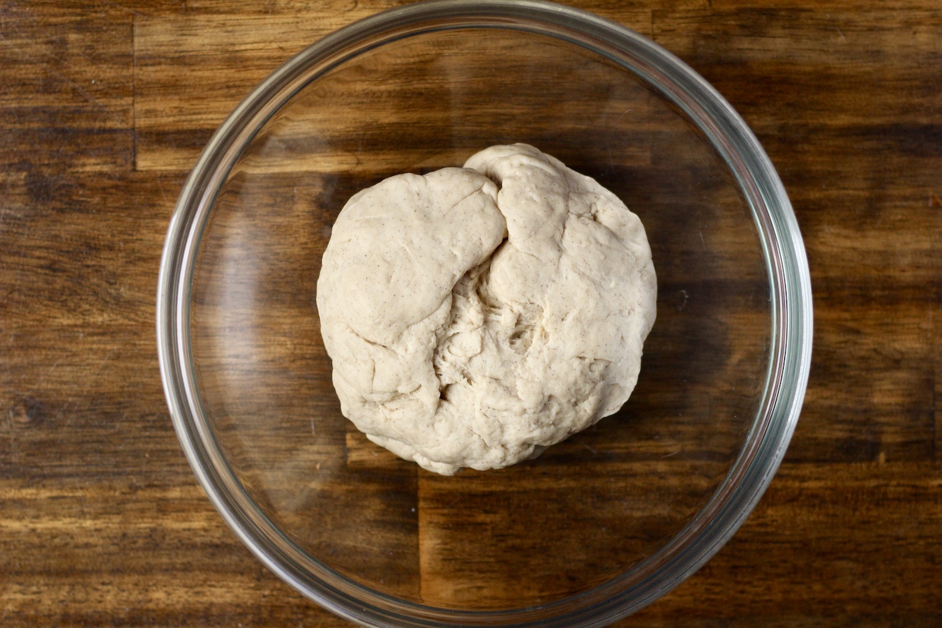 The cinnamon roll dough in a glass bowl on the wooden table.