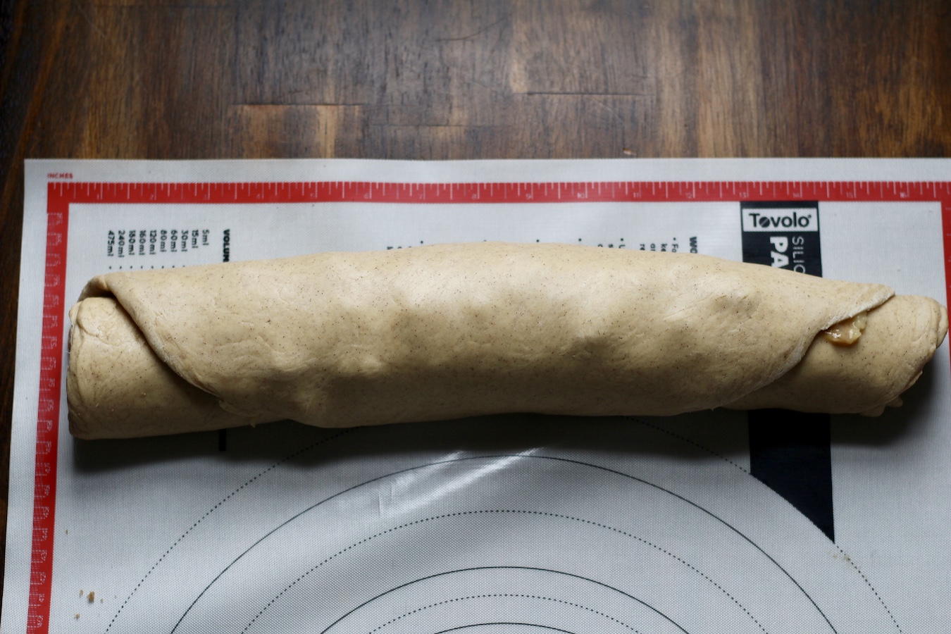 The banana bread cinnamon rolls rolled up on a pastry mat on a wooden table.