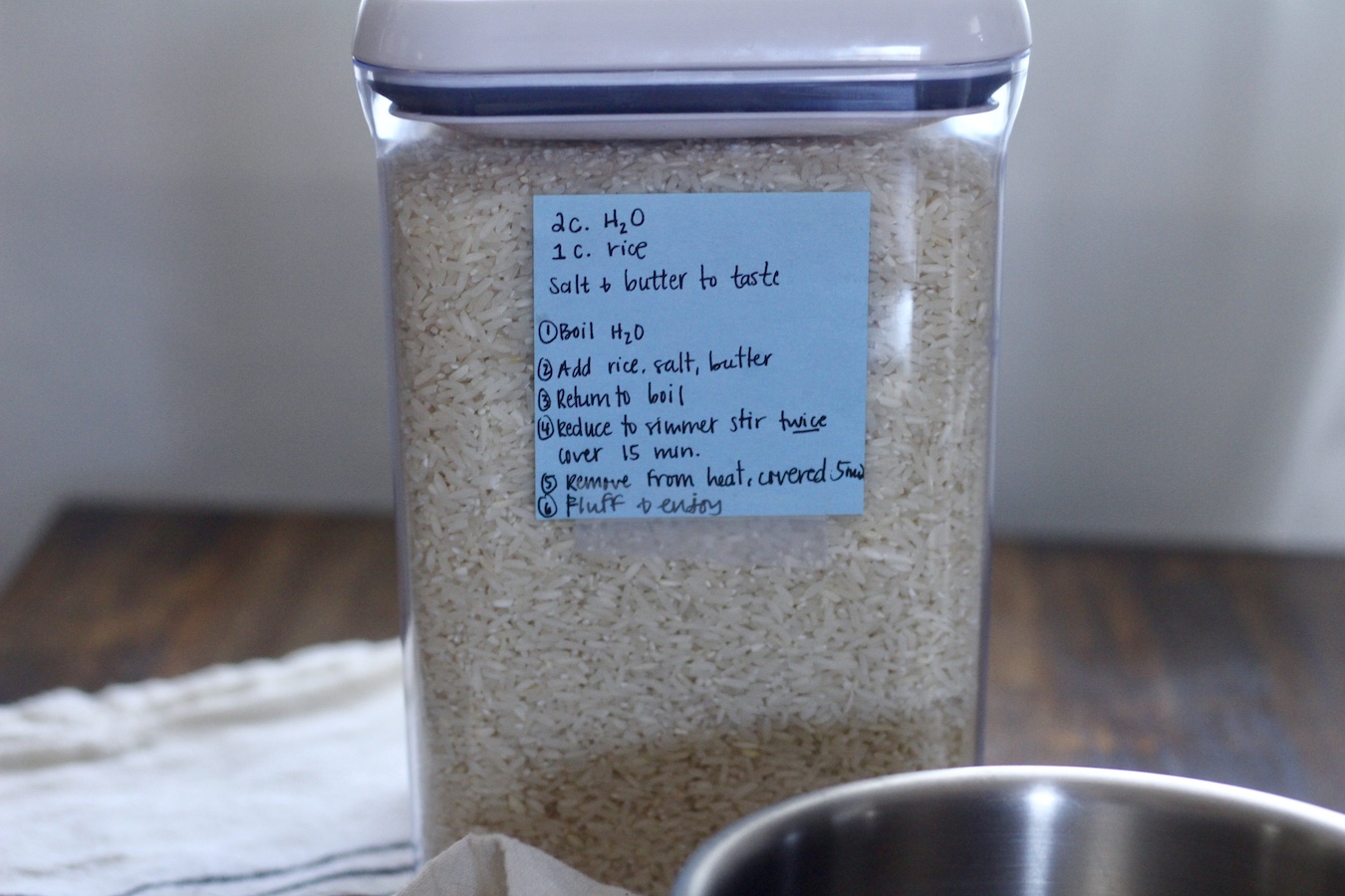 A plastic tupperware with rice and the instructions to cook rice on a blue post it note.