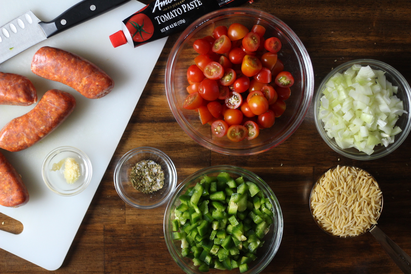 Ingredients to make sausage and orzo pasta in glass bowls and on a cutting board.