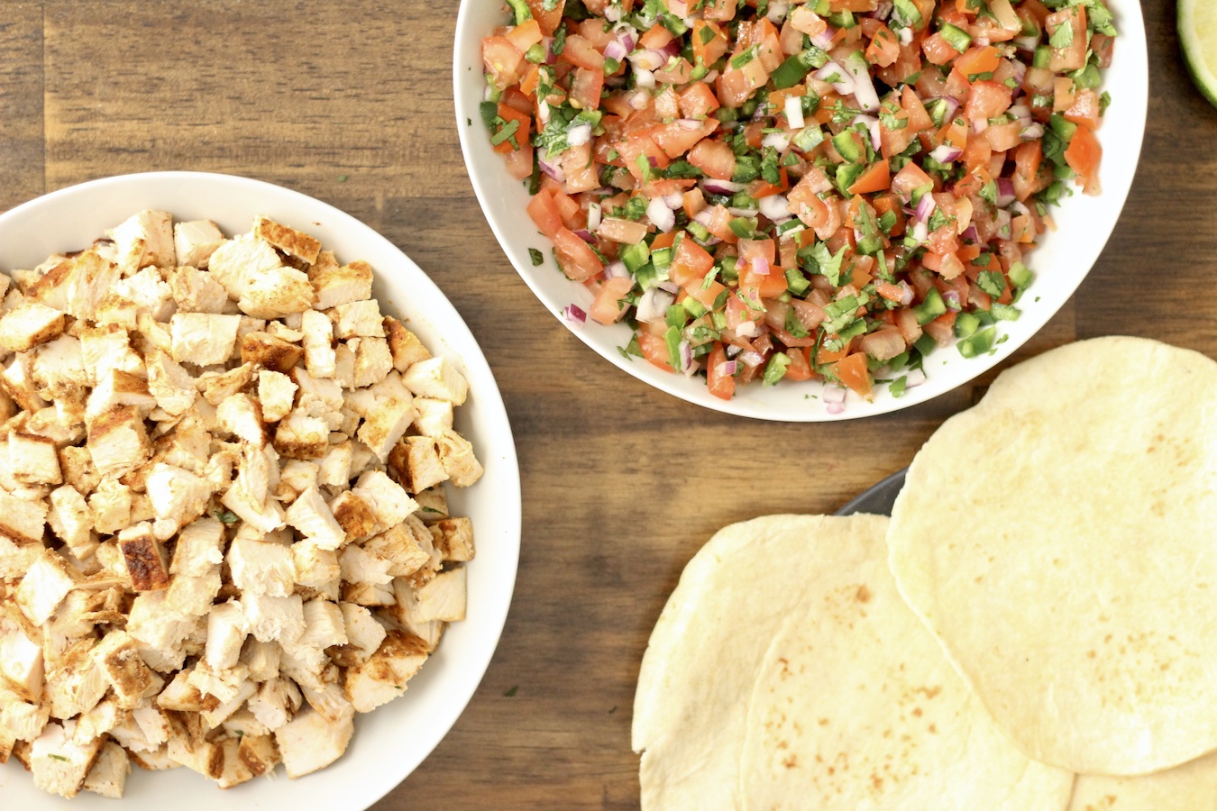 A white bowl with chopped southwest chicken next to a plate of tortillas and a bowl of pico de gallo.