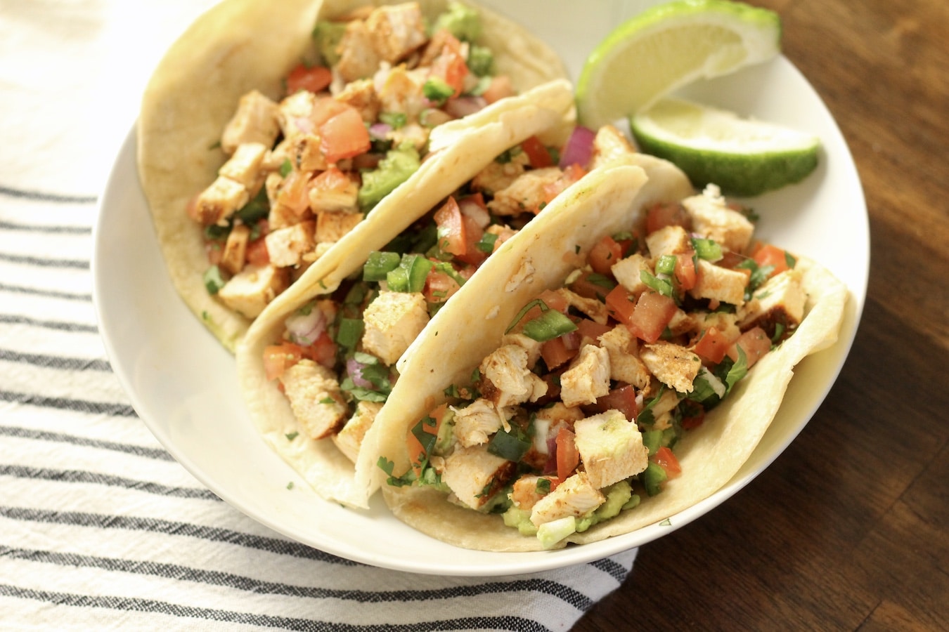 Three southwest chicken tacos on a wooden table with a blue and white towel to the left.
