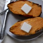 One sweet potato cut lengthwise with vegan butter and salt and a fork and knife the left.