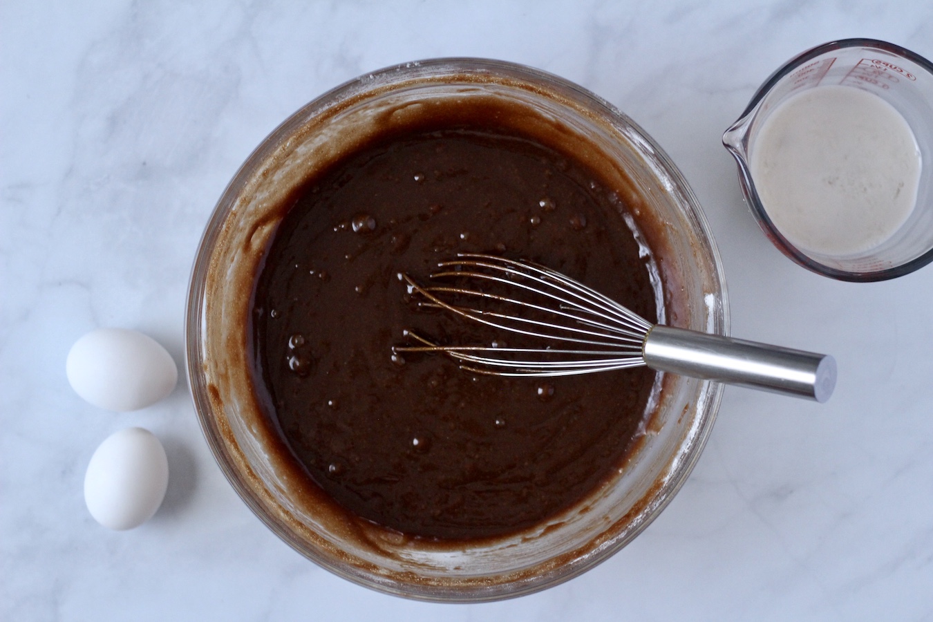 Two eggs next to the chocolate flour mixture and a liquid measuring cup of non dairy buttermilk.