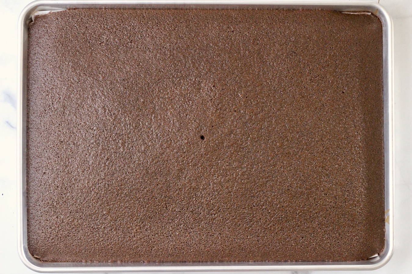 Chocolate sheet cake fresh out of the oven with a hole poked in the middle from testing if it was done.