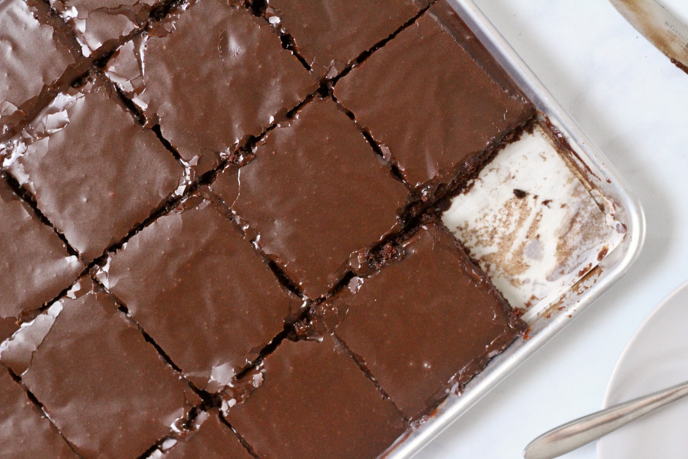 A sheet pan with a square of Texas Sheet Cake cut out and a square where it's missing in the bottom right corner.