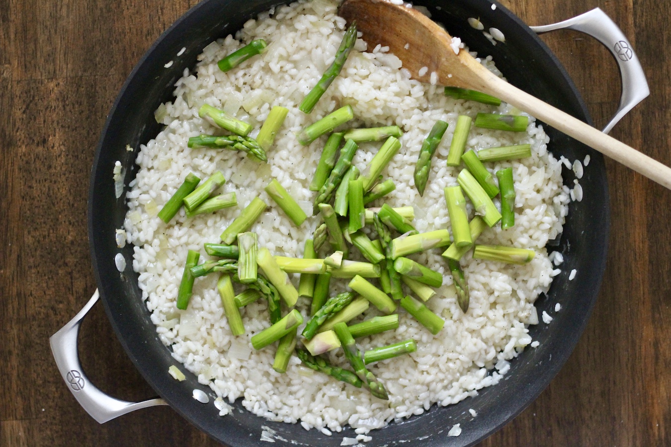 Adding the blanched asparagus to the top of the skillet with the risotto.