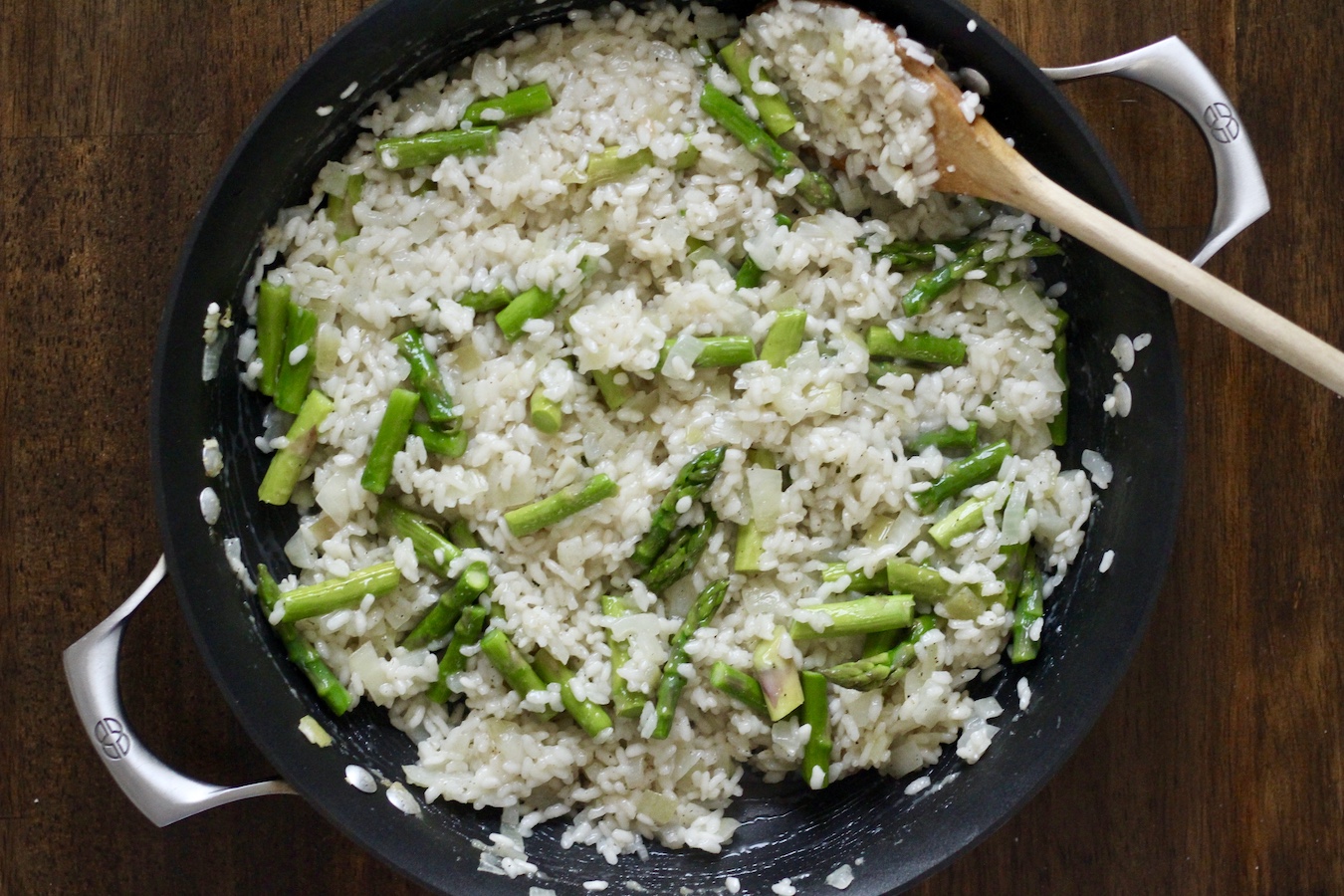 Finished asparagus risotto in a non-stick skillet with a wooden spoon.