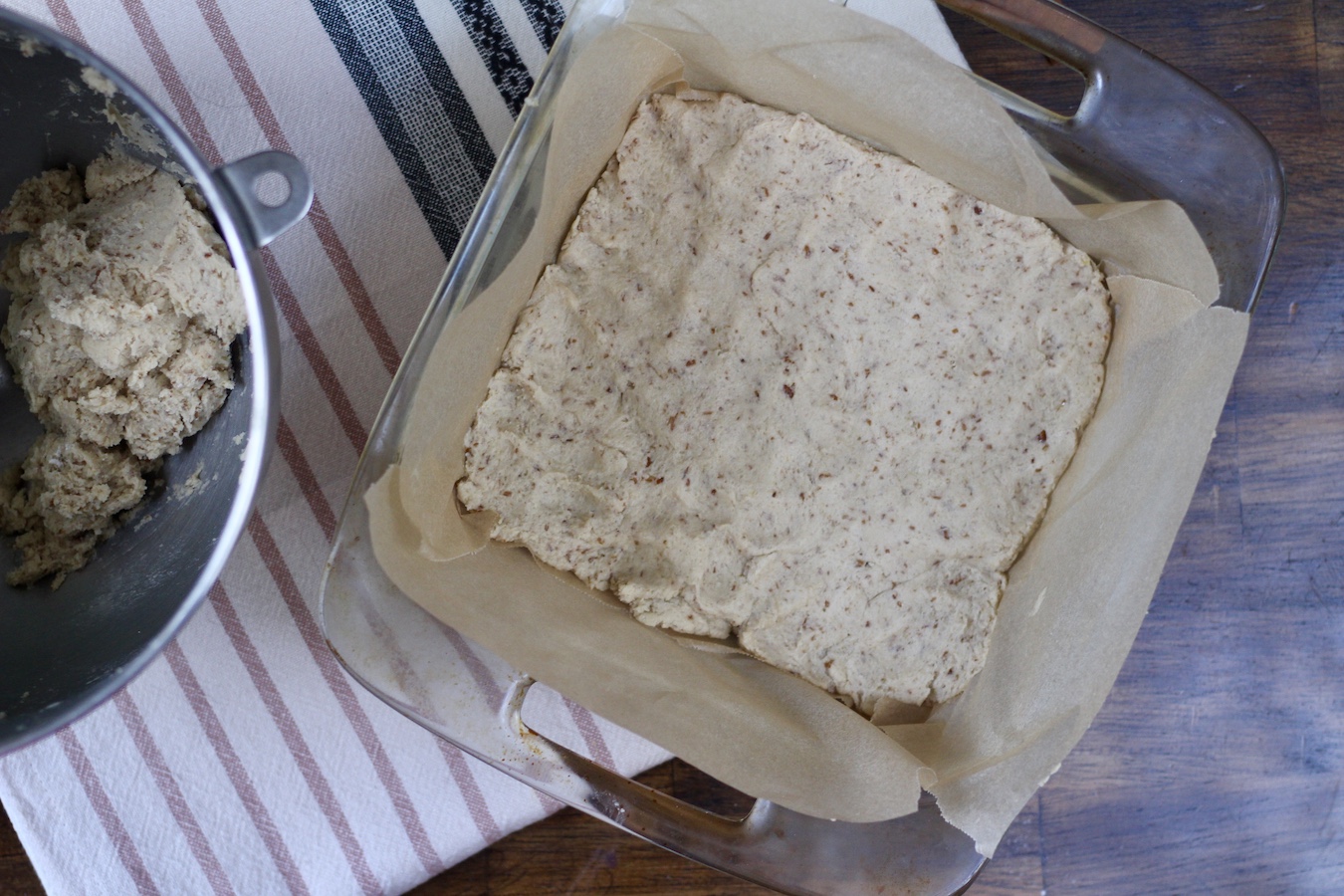 Dough pressed into the parchment paper lined baking dish on a striped dish towel.
