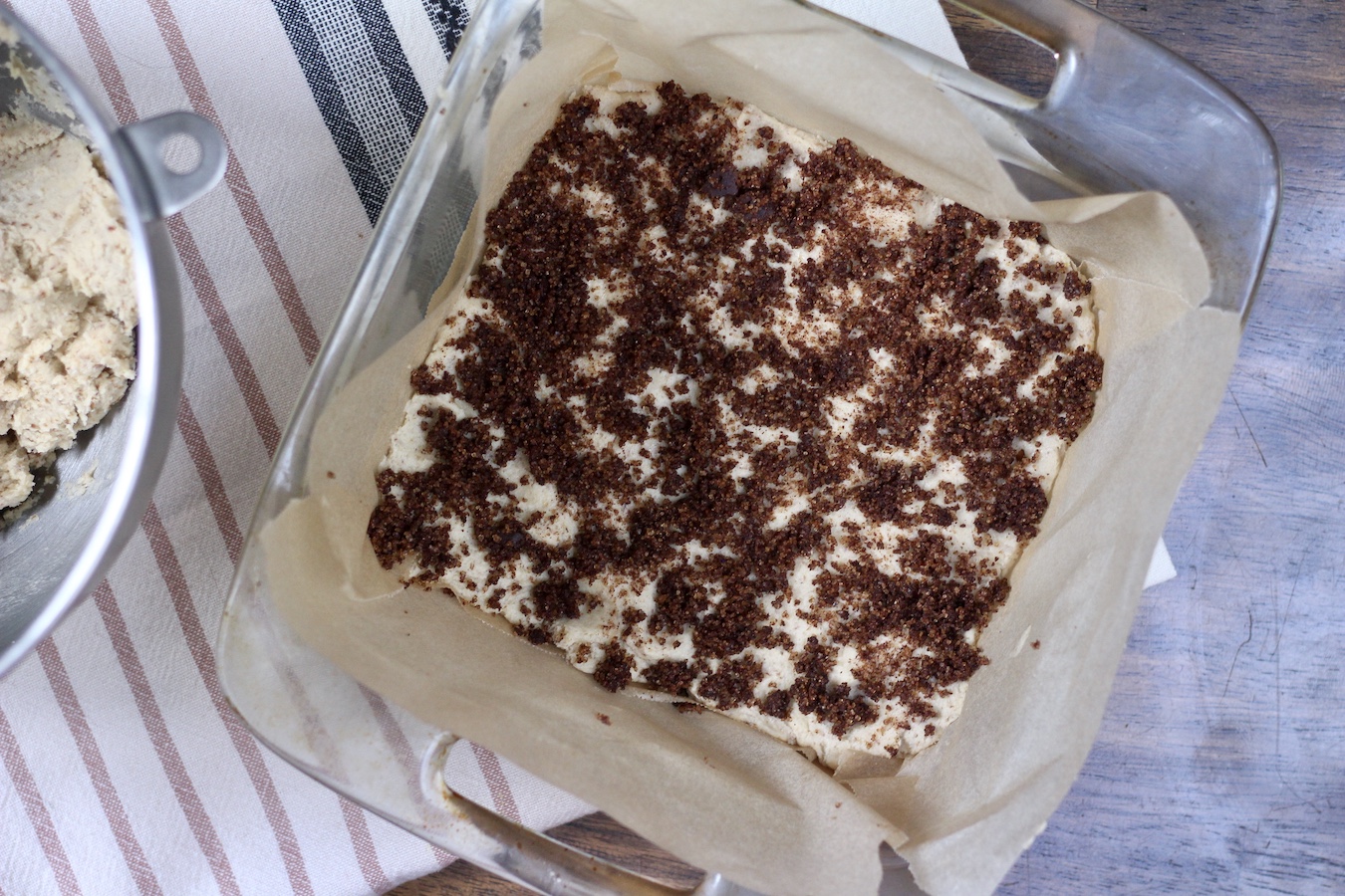 Cinnamon sugar crumble on the first layer of cookie dough batter in the baking dish on a striped towel.