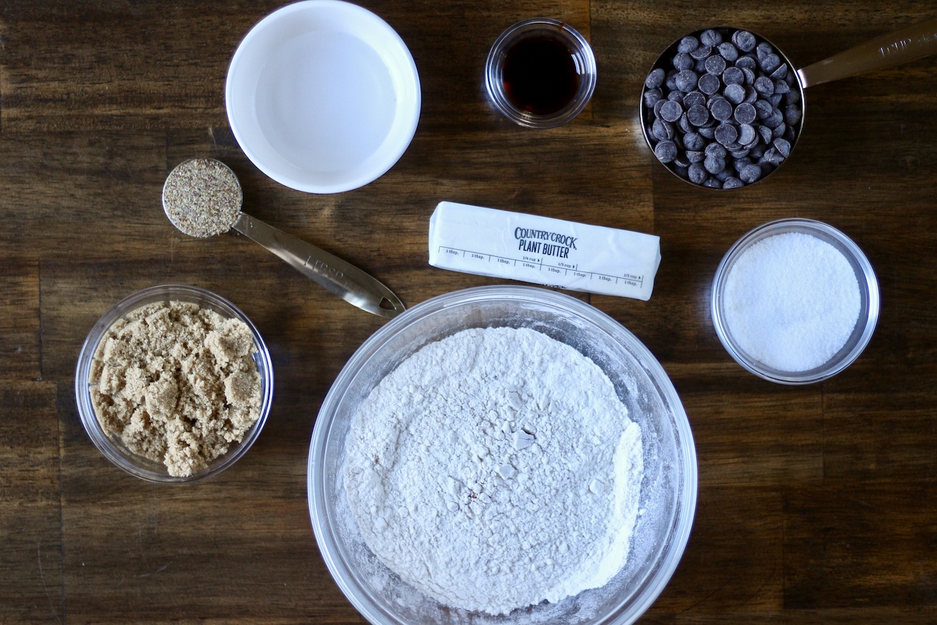 Ingredients to make egg free chocolate chip cookies on a wooden table.