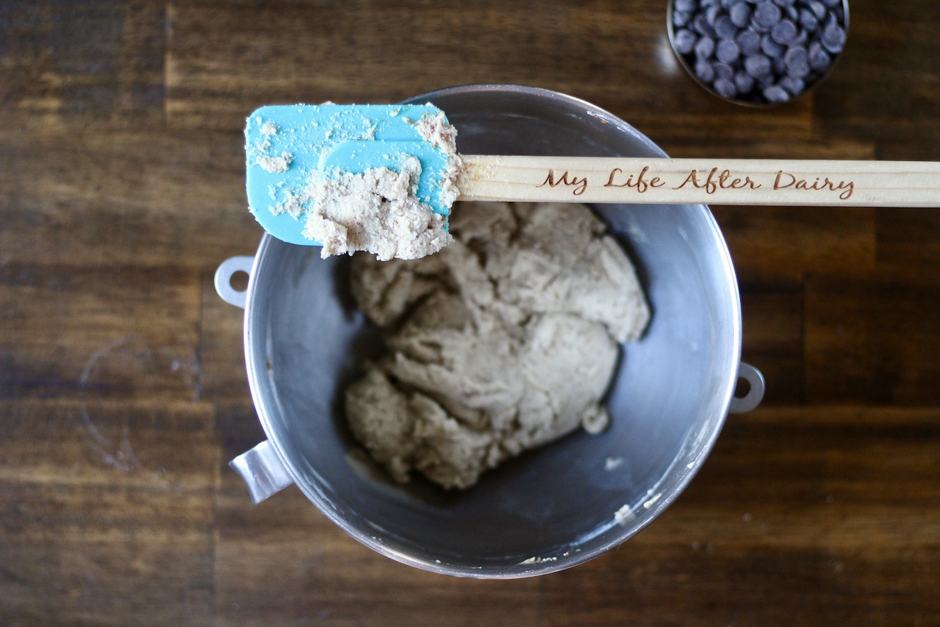 A spatula with the words my life after dairy on the handle on a mixing bowl with egg free cookie dough on a wooden table.