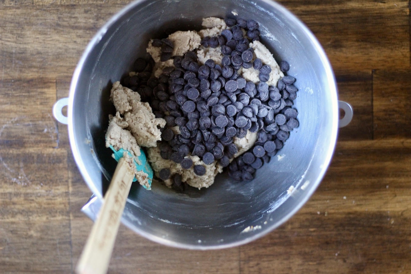 Chocolate chips on top of egg free cookie dough in a mixing bowl on a wooden table.